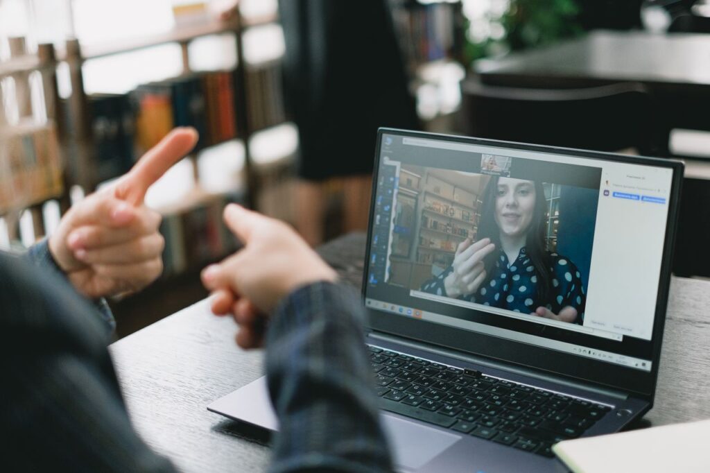 Crop anonymous woman teaching sign language to female student during video call via laptop in light workspace